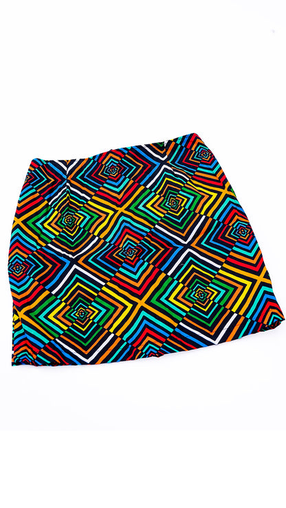 Minifalda sastrera estructurada confeccionada con auténtica tela africana Ankara, presentando un vibrante patrón geométrico de cuadrados concéntricos en capas de colores rojo, amarillo, verde, azul y negro. La falda tiene tiro alto, cierre posterior central de cremallera roja visible y corte evasé, capturada contra un fondo blanco limpio,y sifisticado