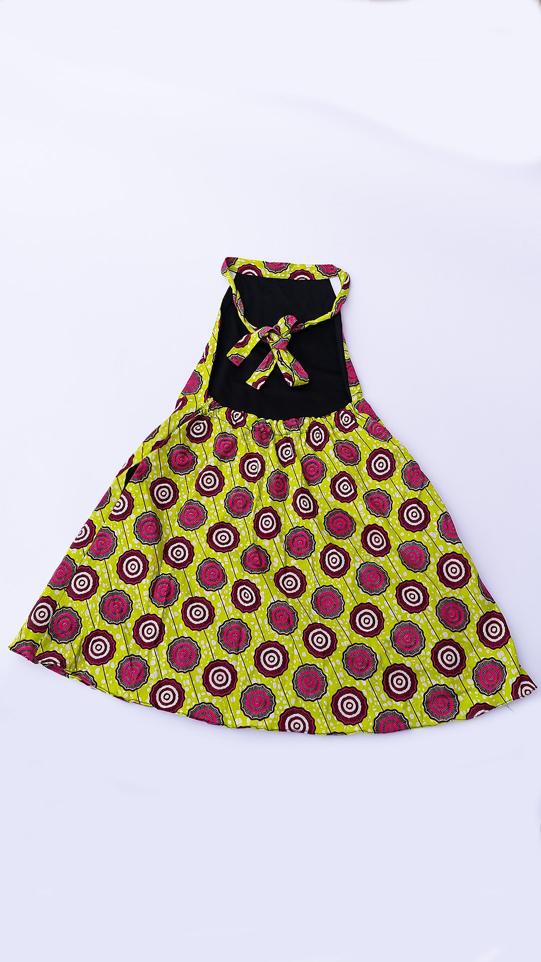 vestido corto estilo halter de corte trapecio, confeccionado en tela Ankara con un patrón vibrante de círculos en fucsia, marrón y blanco sobre fondo amarillo lima.