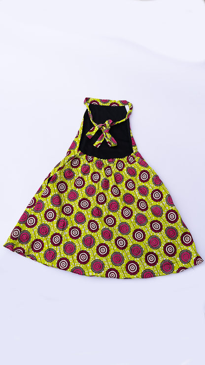 vestido corto estilo halter de corte trapecio, confeccionado en tela Ankara con un patrón vibrante de círculos en fucsia, marrón y blanco sobre fondo amarillo lima.