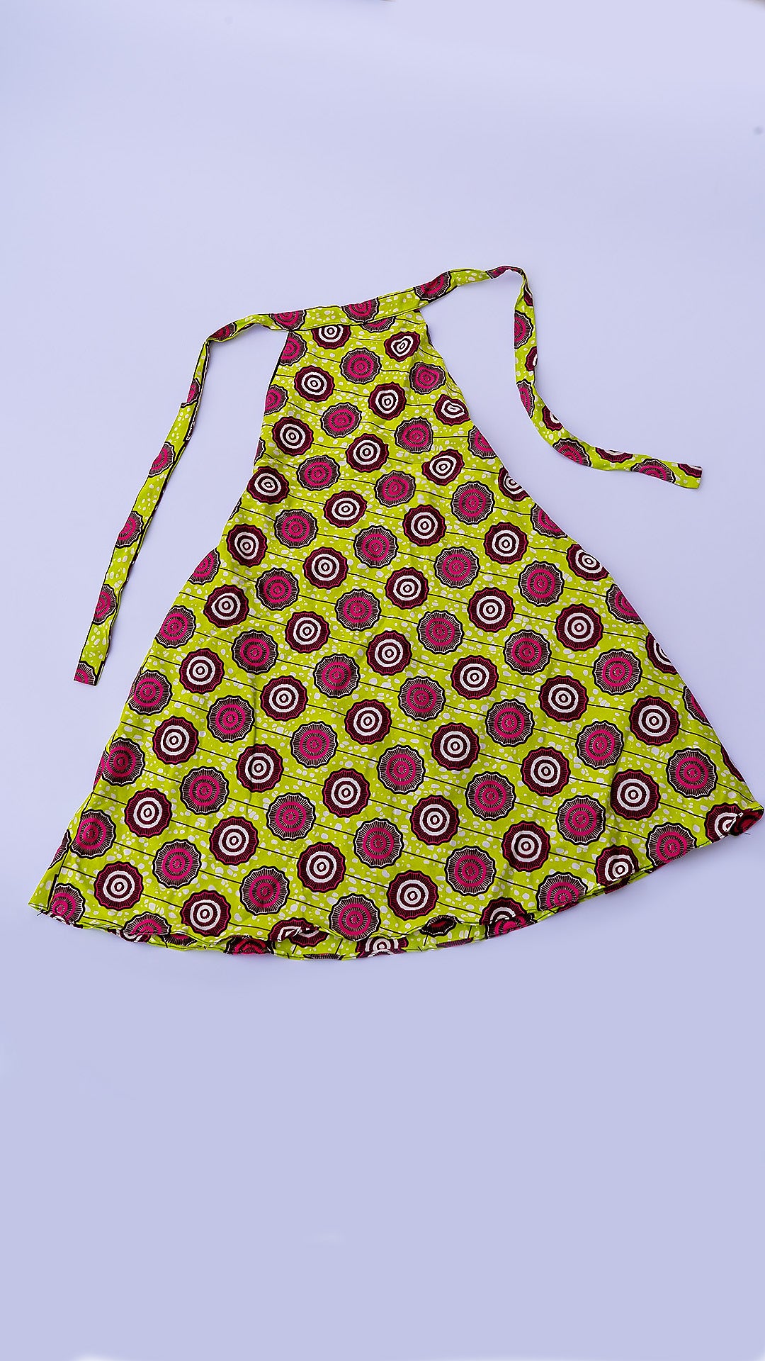 vestido corto estilo halter de corte trapecio, confeccionado en tela Ankara africana con un patrón vibrante de círculos en fucsia, marrón y blanco sobre fondo amarillo lima.