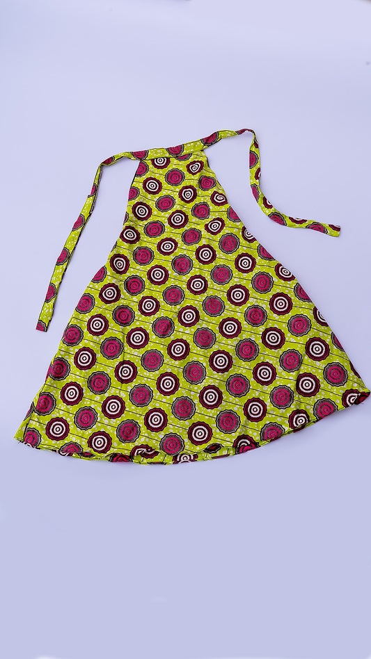 vestido corto estilo halter de corte trapecio, confeccionado en tela Ankara africana con un patrón vibrante de círculos en fucsia, marrón y blanco sobre fondo amarillo lima.